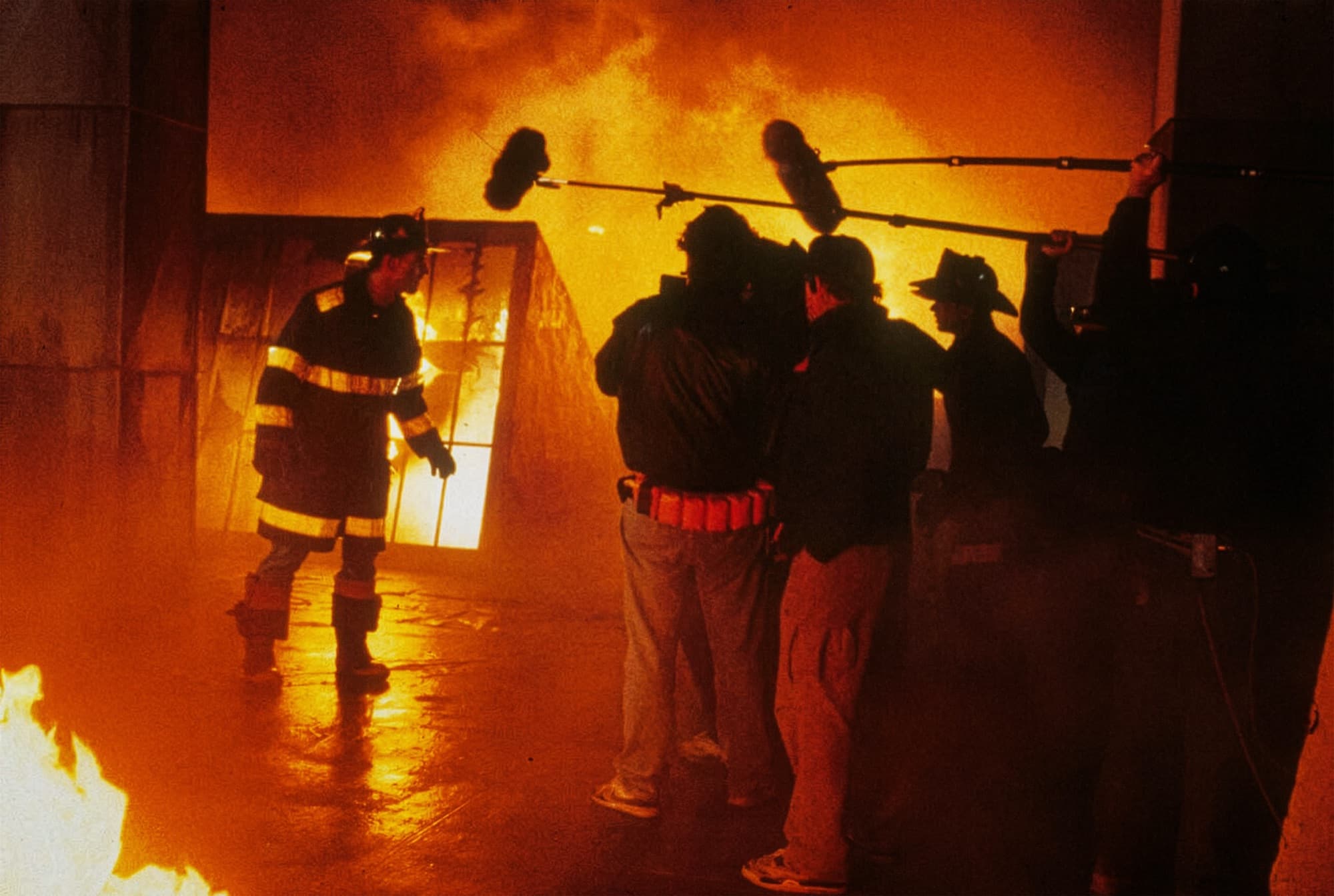 A film crew with boom microphones in front of a burning set.